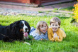 funny children lying on the grass with bernese mountain dog
